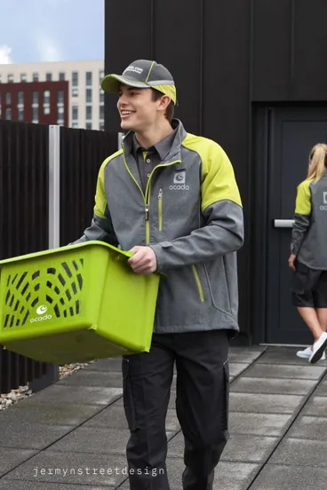 Facility services worker in a grey and lime jacket carrying a basket