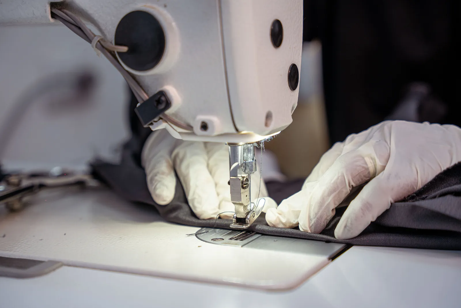 Gloved hands guiding fabric under a sewing machine